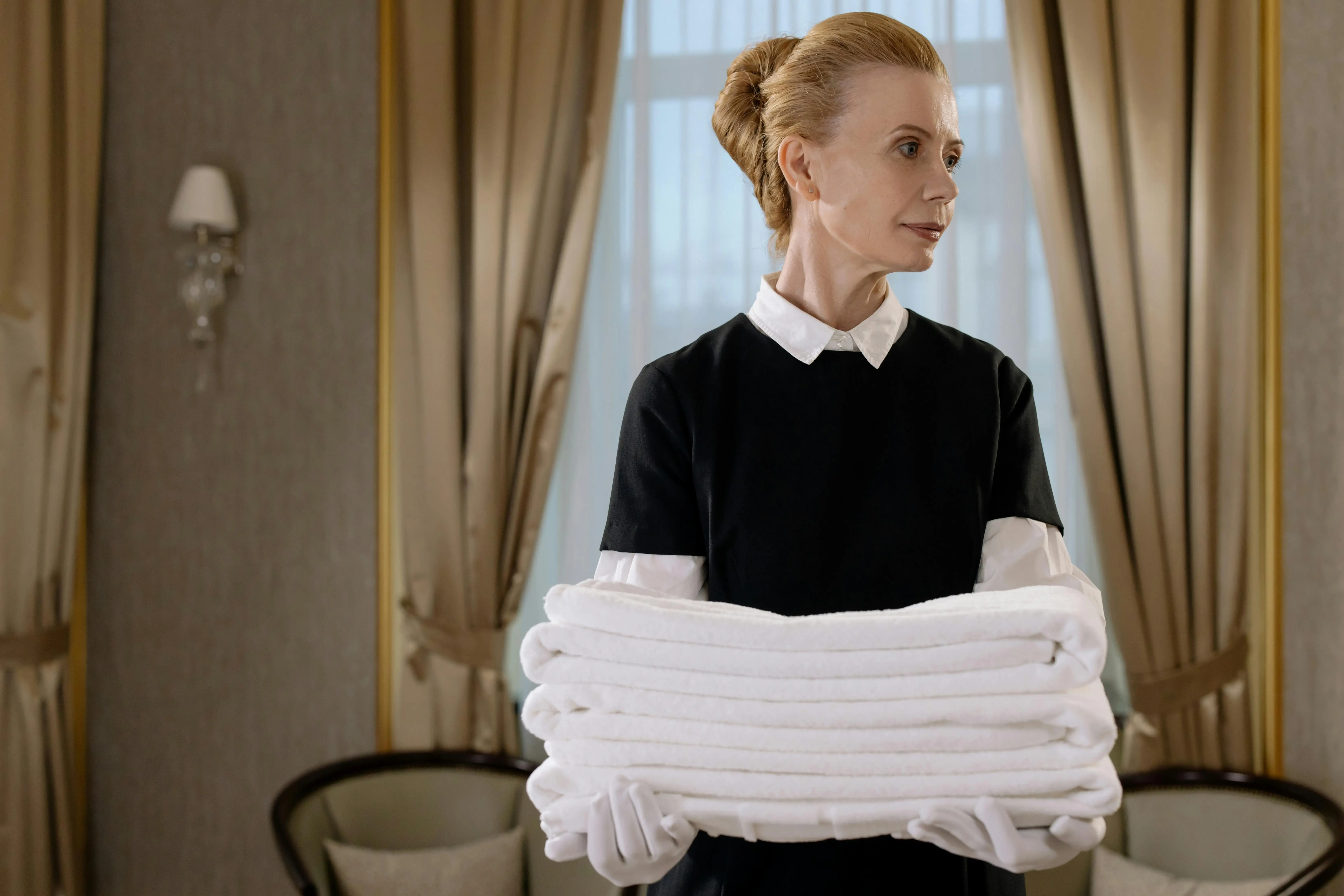 a maid caring the blanket in her hand and looking right wearing the maid uniform in dubai